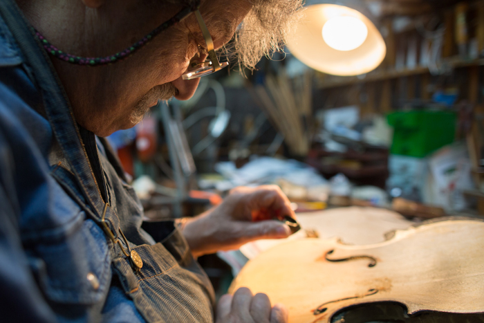 Amnon Weinstein using a minute luthier plane to delicately carve the back of the top of a Holocaust violin in order to improve its pitch and resonance to its highest sound quality. 