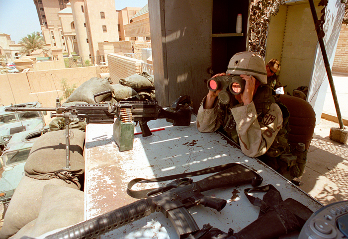 An American soldier scans the streets with binoculars at a guard post in downtown Baghdad, Iraq, July 2003.
